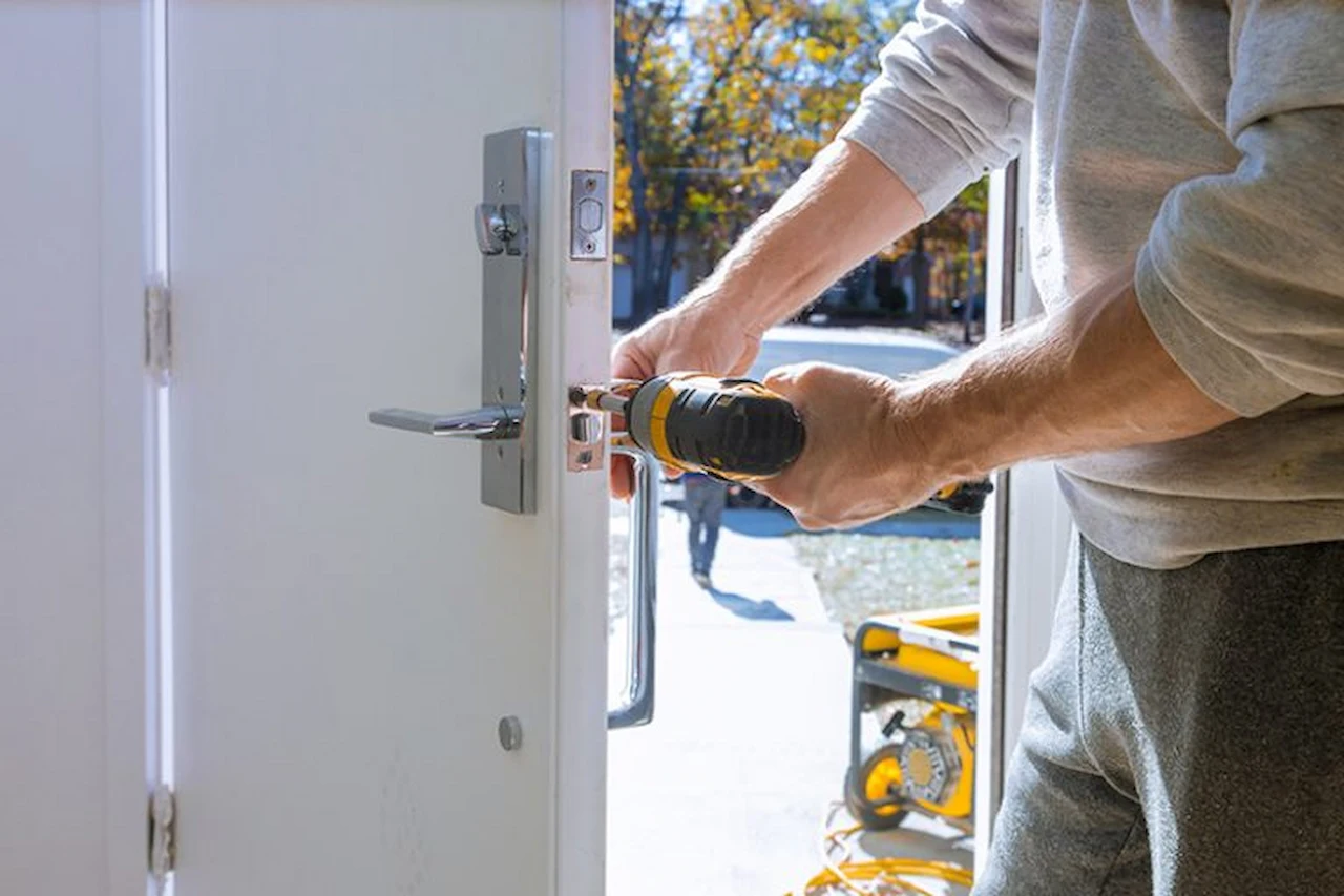Technician using a power drill to install or repair a front door lock.