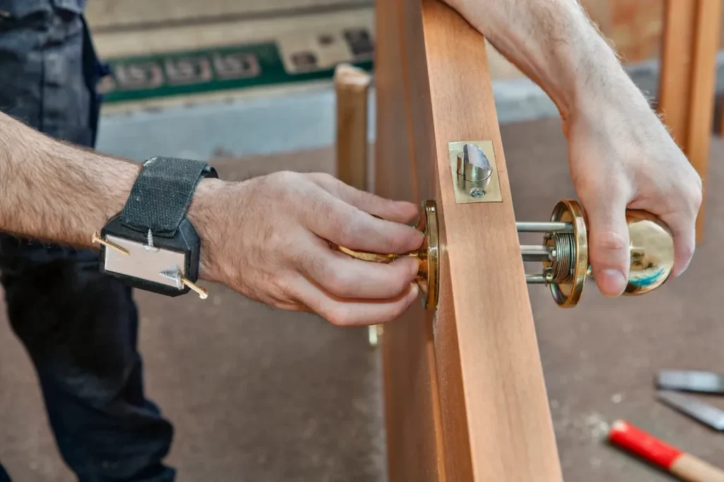 Technician installing a door handle and lock mechanism on a wooden door.